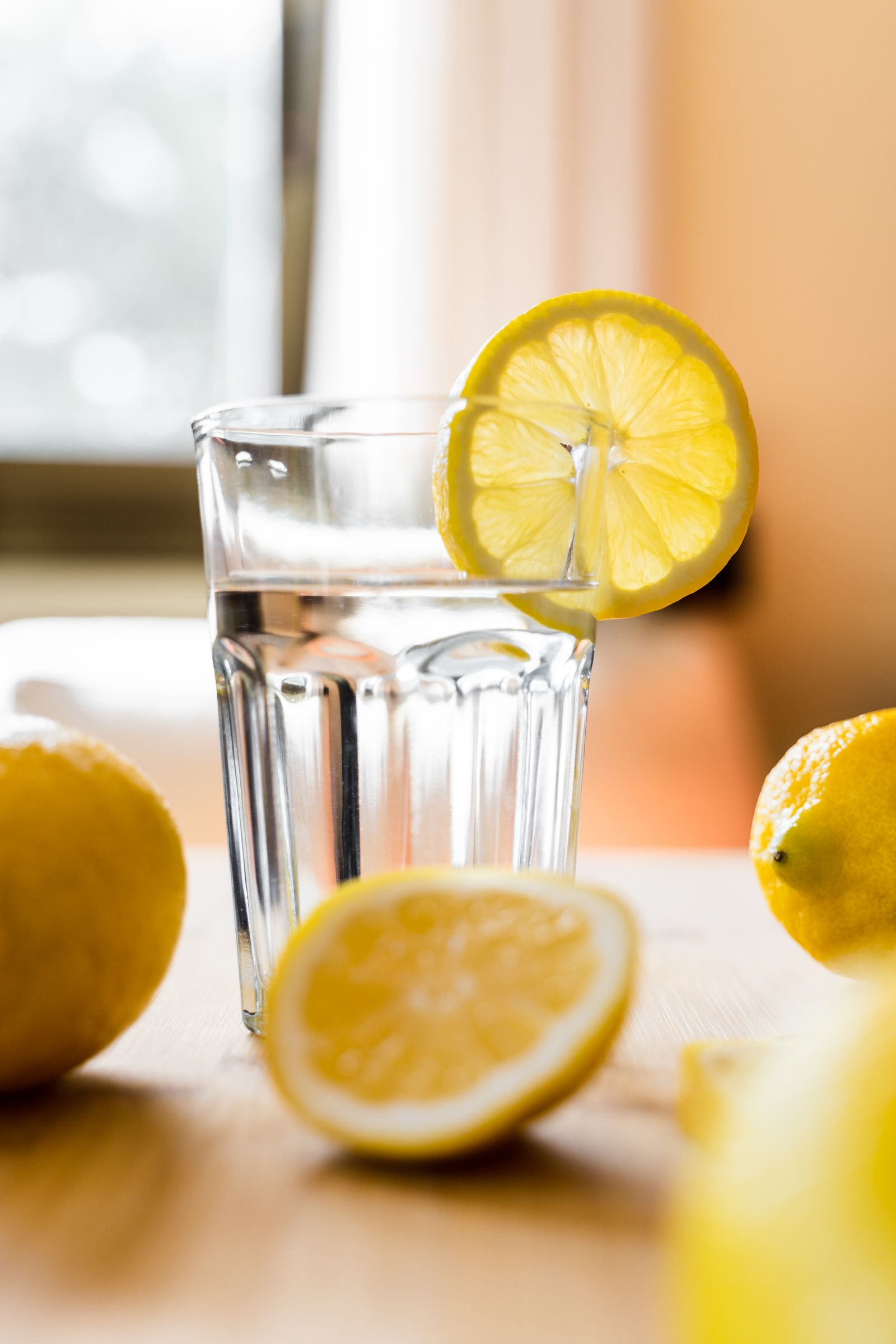 A tall glass of clear water with a slice of lemon on a light wooden table.