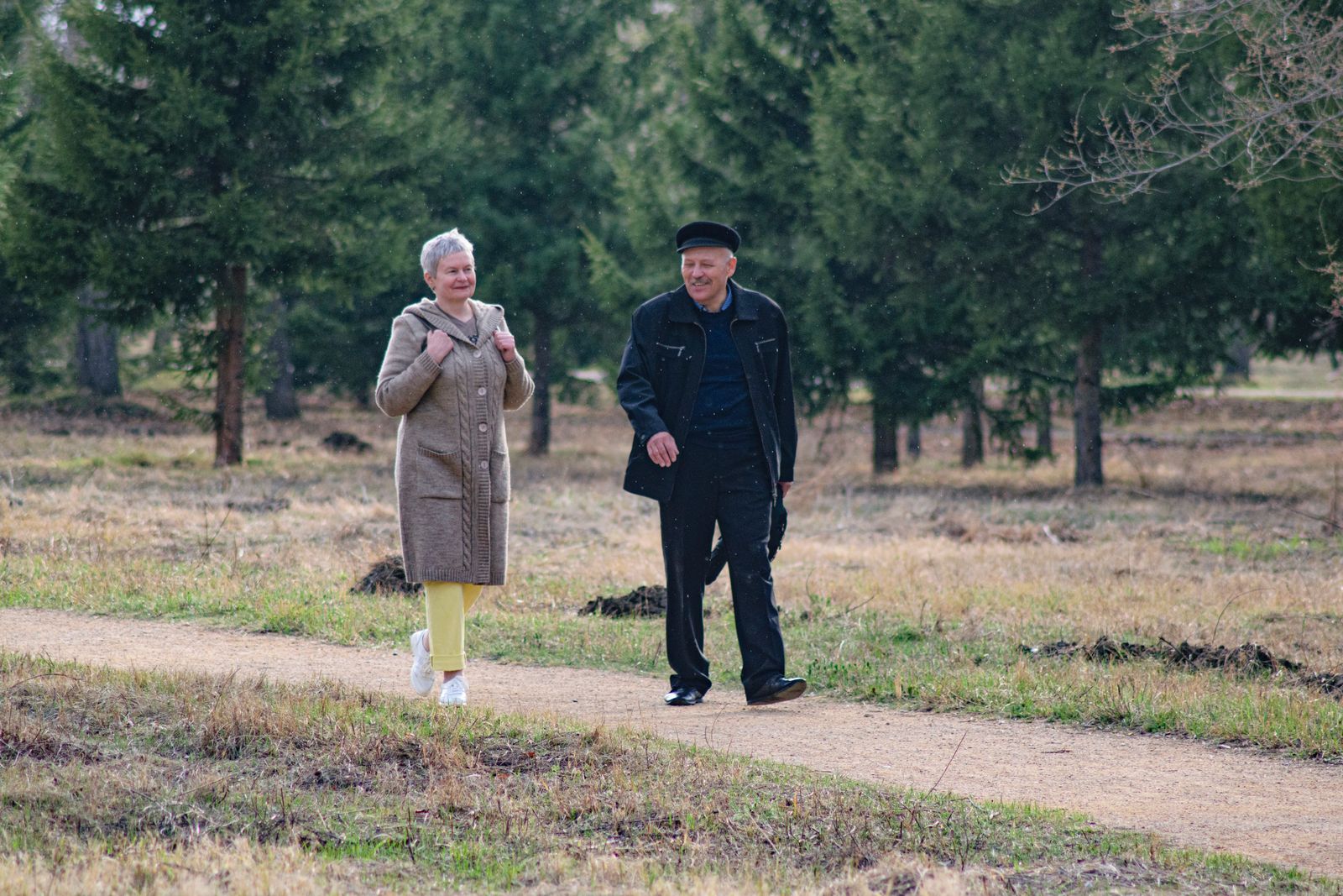 A couple in their sixties walking briskly along a country path in the fresh air.